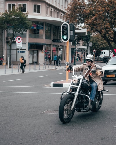 穿黑夹克的男子白天在路上骑摩托车